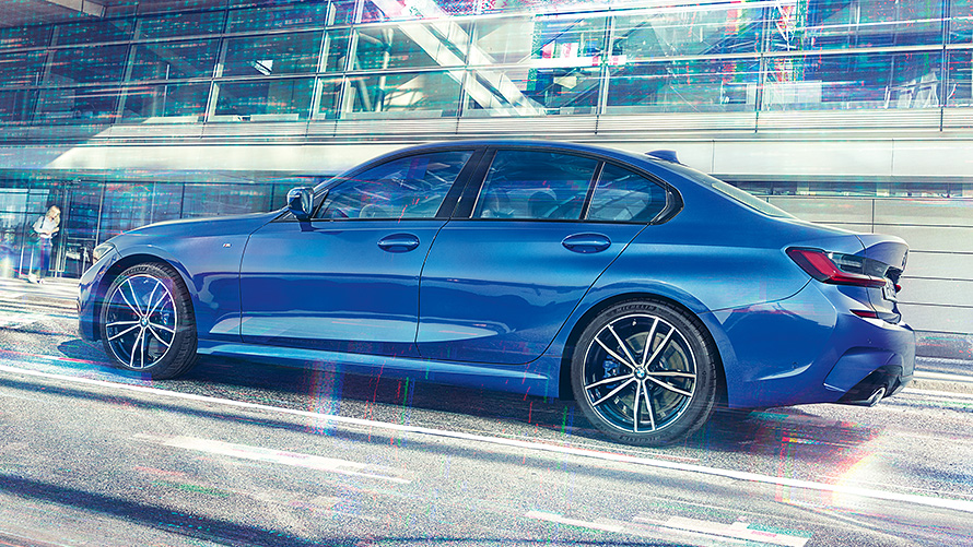 Static side view of the BMW 3 Series Sedan (G20) Portimao Blue during day in front of building made of glass.